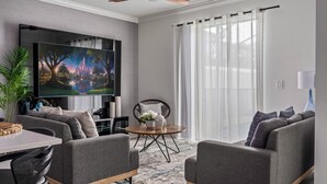 A modern living room with a flat-screen TV, grey sofas, a coffee table, and a ceiling fan.
