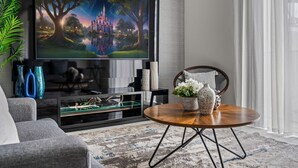 A modern living room with a flat-screen TV, a round wooden coffee table, and a comfortable sofa.