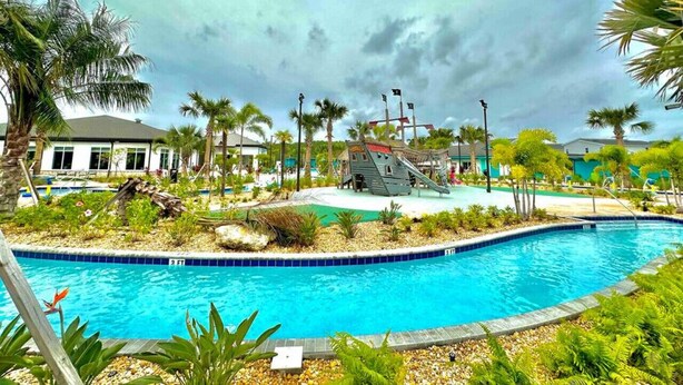 A swimming pool with a slide, palm trees, and a building in the background.