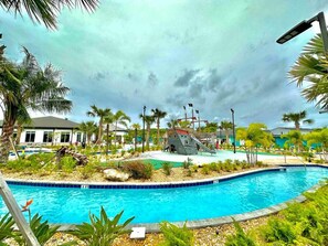 A swimming pool with a slide, palm trees, and a building in the background. - Elegant and Cozy pool bbq (Kissimmee)