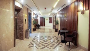 A hotel lobby with a marble floor, a reception desk, and a seating area with chairs and a table. - EMAAR INTERNATIONAL (Makkah)