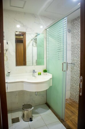 A bathroom with a white sink, a mirror, a small potted plant, and a shower with a glass door.