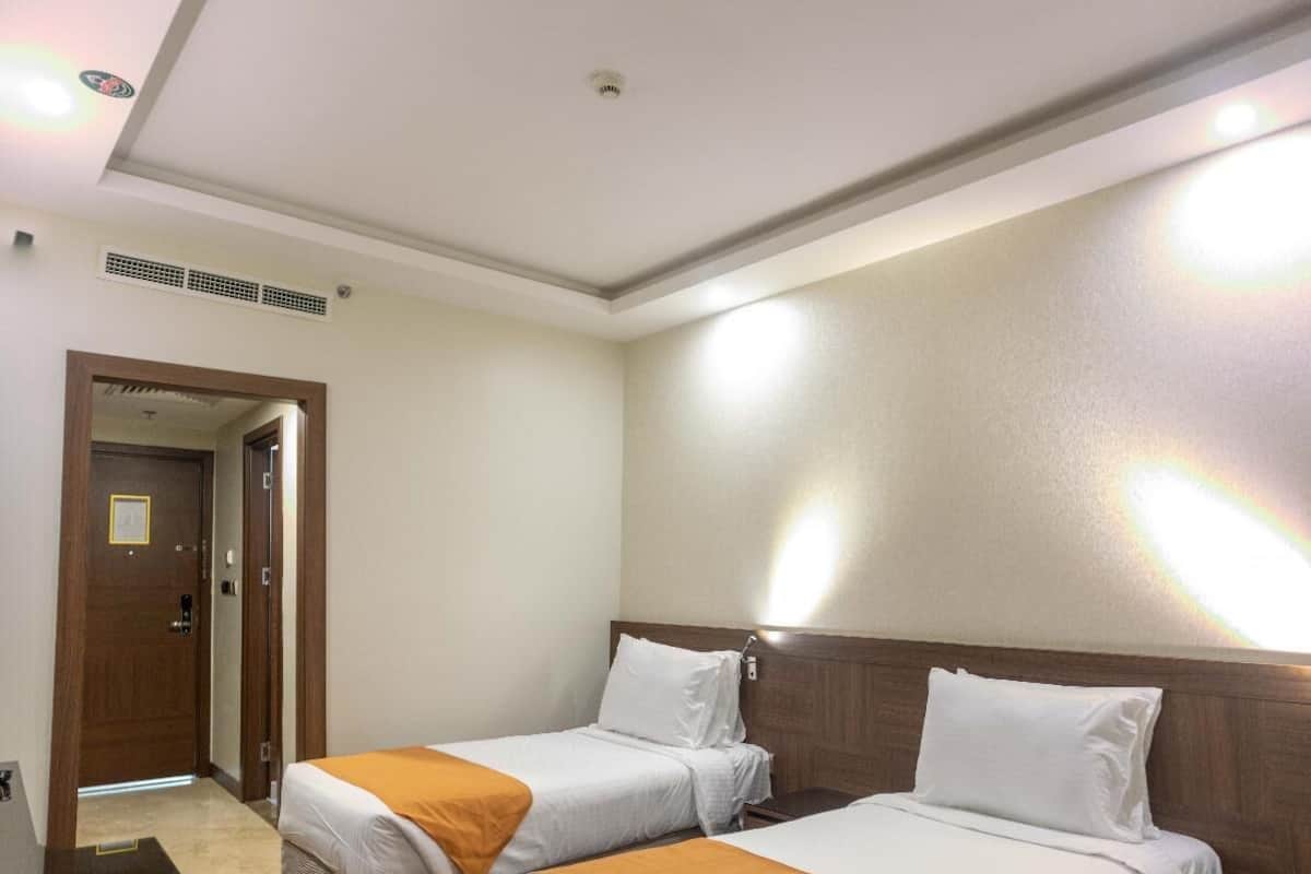 A hotel room with two beds, a wooden headboard, a mirror, and a small table with a vase.