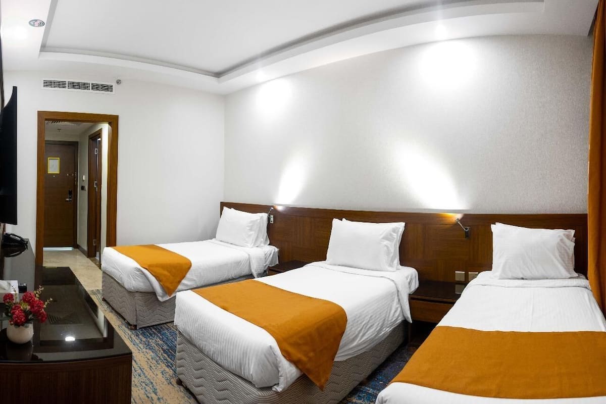 A hotel room with three beds, a desk with a telephone, and a television.