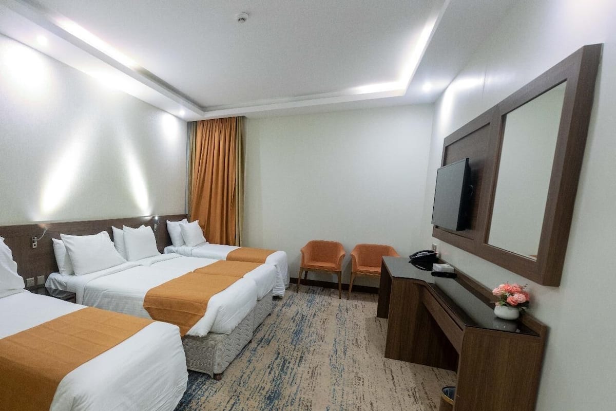 A hotel room with three beds, a desk, a chair, a TV, and a mirror.