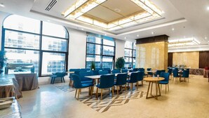 A spacious hotel lobby with large windows, blue seating, and a modern chandelier. - EMAAR INTERNATIONAL (Makkah)
