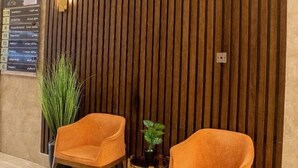 A reception area with two orange chairs, a small table, a potted plant, and a wooden slat wall. - EMAAR INTERNATIONAL (Makkah)