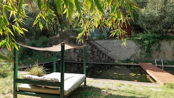 Un letto sotto una tenda con vista su uno stagno e un muro in pietra.