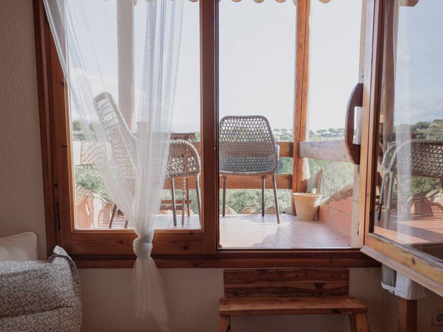 A bedroom with a bed, a wooden chair, and a window overlooking a patio with a chair and a table.