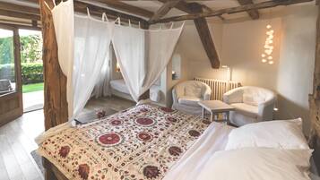 A bedroom with a large bed, a chair, a table, and a window with curtains.