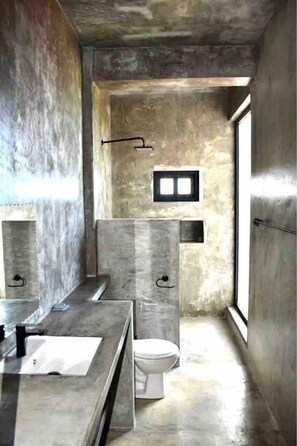 Een badkamer met een betonnen vloer, een toilet en een raam voor natuurlijk licht.