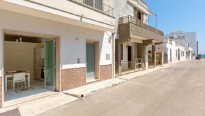 Une rue résidentielle bordée de maisons dotées de balcons, avec un regard d’égout visible et une vue dégagée sur la mer en arrière-plan.