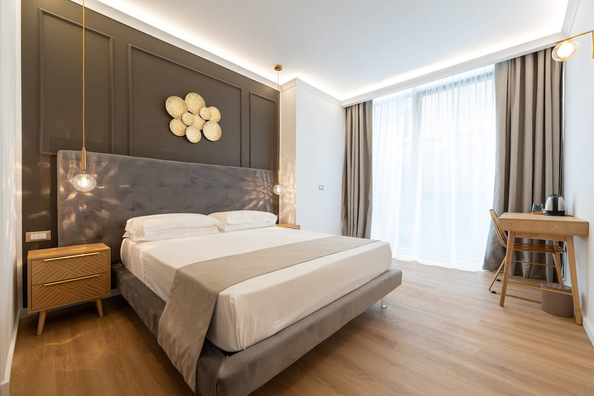 A modern bedroom with a large bed, bedside tables, a desk, and a large window with curtains.