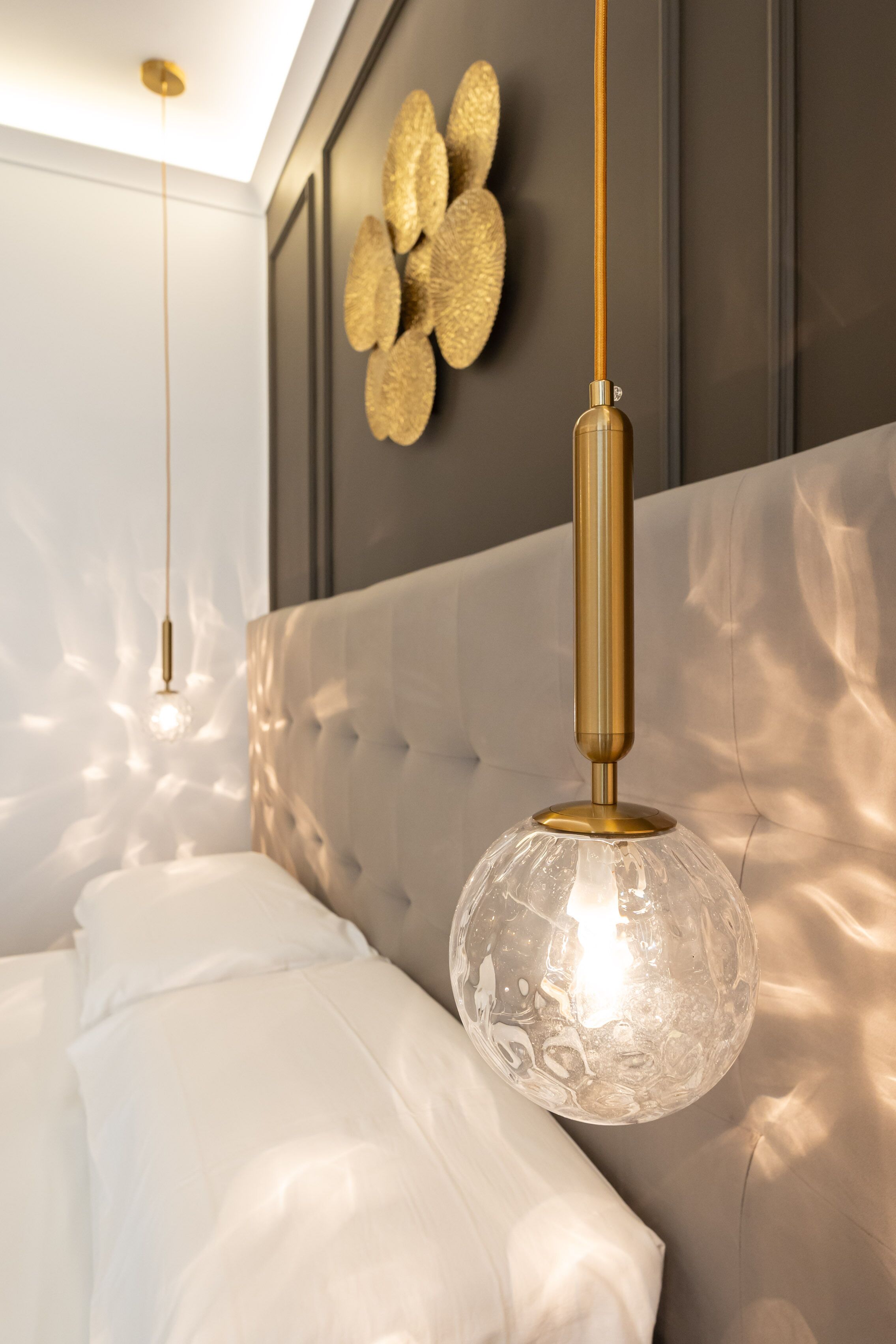 A bedroom with a tufted headboard, a hanging light fixture with a clear glass shade, and a wall-mounted decorative piece.