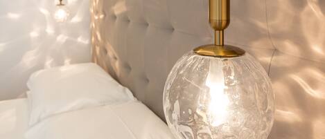 A bedroom with a tufted headboard, a hanging light fixture with a clear glass shade, and a wall-mounted decorative piece.