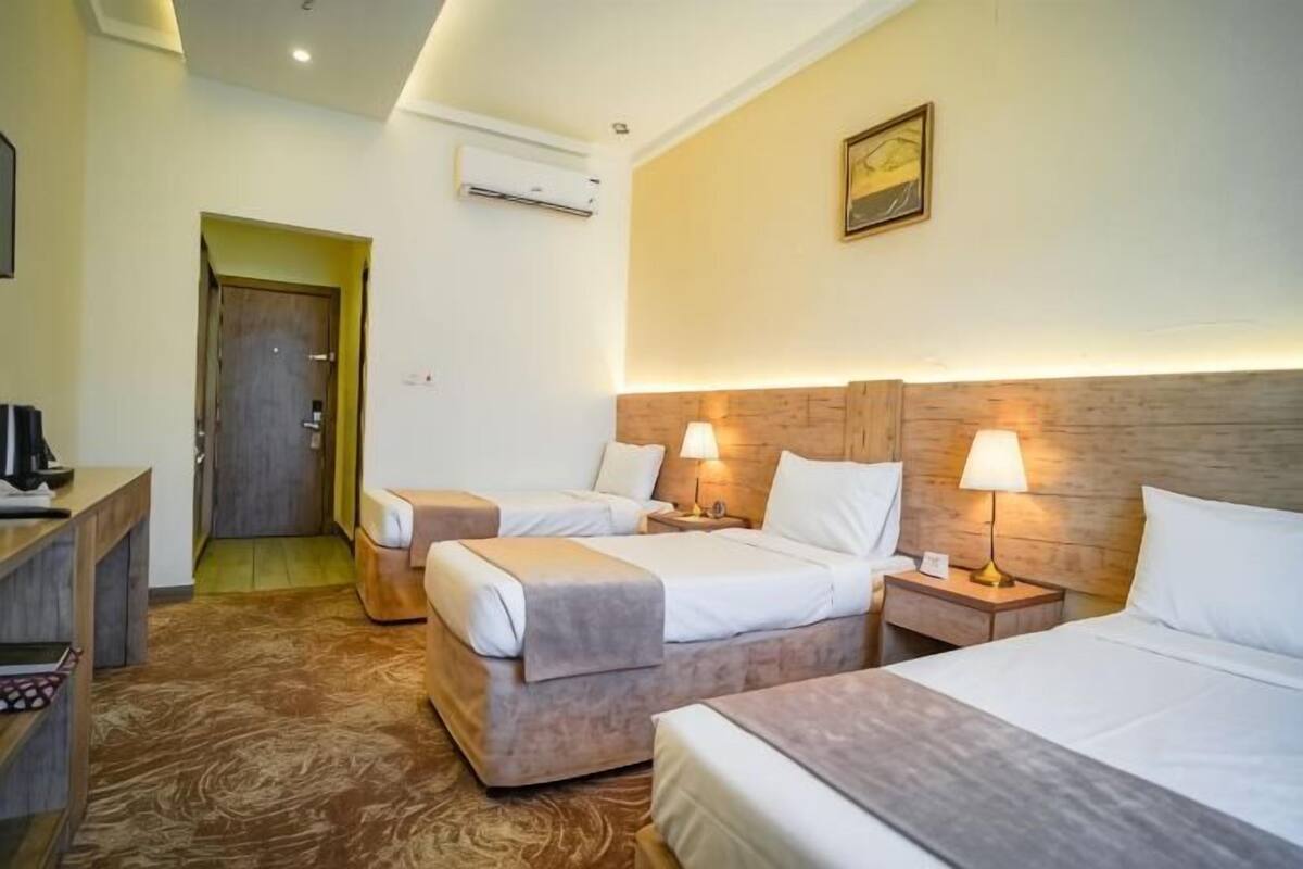 A hotel room with three beds, a desk, and a door leading to another room.