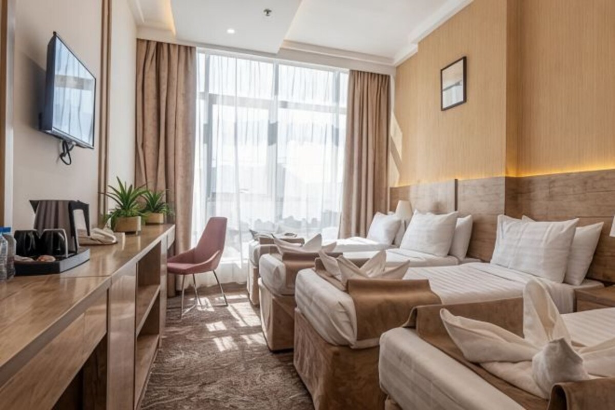 Habitación de hotel con cama, escritorio con silla, televisor y ventana con cortinas.