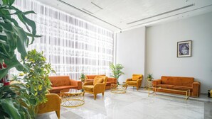 Um hall moderno com uma grande janela, sofás laranja e plantas em vasos.