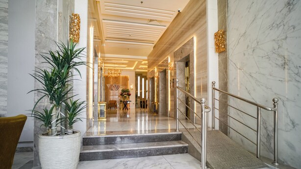 Um hall com piso de mármore, uma escadaria, uma planta em vaso grande e uma cadeira dourada.