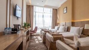Quarto de hotel com cama, escrivaninha, cadeira, televisão e janela com cortinas.
