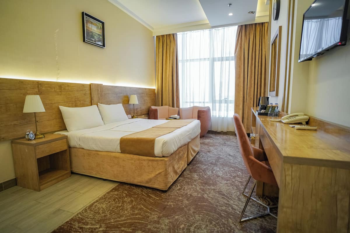 A hotel room with a large bed, a desk with a telephone, a chair, and a TV mounted on the wall.