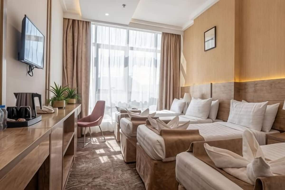 A hotel room with a bed, a desk with a chair, a TV, and a window with curtains.