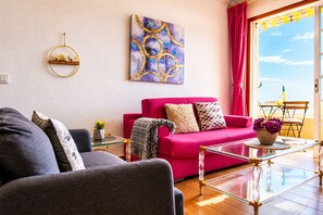 A living room with a red sofa, a glass coffee table, and a painting on the wall.