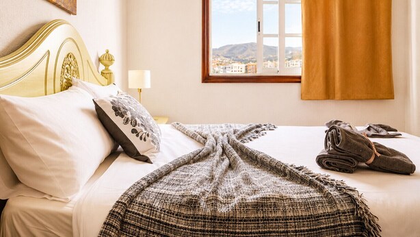 Ein Hotelzimmer mit Bett, Blick auf die Stadt durch ein Fenster und einem Vorhang.