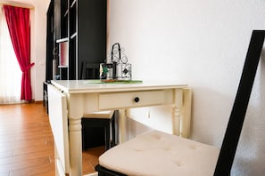 A white desk with a drawer, a black chair, and a red curtain in a room with wooden flooring.