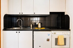 A compact kitchen with a sink, kettle, and a small oven.
