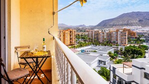 Ein Balkon mit Tisch, Stühlen und einer Weinflasche, mit Blick auf eine Stadtlandschaft aus Wohnhäusern und Bergen.