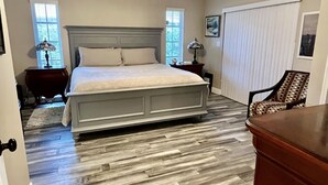 Un dormitorio con cama, ventilador de techo, mesita de noche, silla y cómoda.