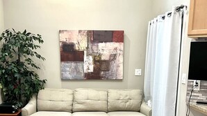 Una sala de estar con un sofá seccional color beige, un pequeño reposapiés, una mesa de comedor de madera y una planta en maceta.