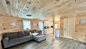 Un interior de madera con un sofá seccional gris, una zona de cocina y una puerta.