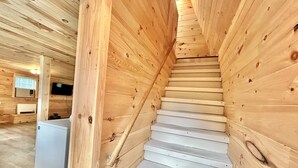 Una escalera de madera en una cabaña con un electrodoméstico blanco y una ventana con persianas.