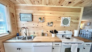 Una cocina compacta con paredes de madera, un lavamanos de acero inoxidable, un lavavajillas y una estufa.