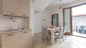 A modern kitchen with a built-in sink and cabinets, a dining area with a table and chairs, and a sliding glass door leading to an outdoor area. - 3494 Vico Roca by Barbarhouse (Melendugno)