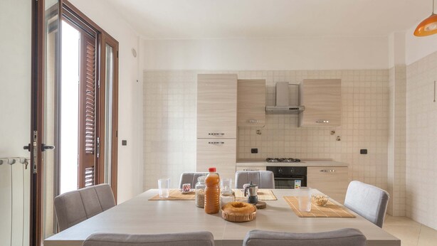 A modern kitchen with a large island, built-in appliances, and a dining area with chairs. - 3494 Vico Roca by Barbarhouse (Melendugno)