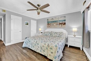 A bedroom with a bed, a ceiling fan, a nightstand, and a beach-themed wall art. - 3BR Gulf Front, Sleeps 10 & Quiet East End | Regency Towers 1121 (Panama City Beach)