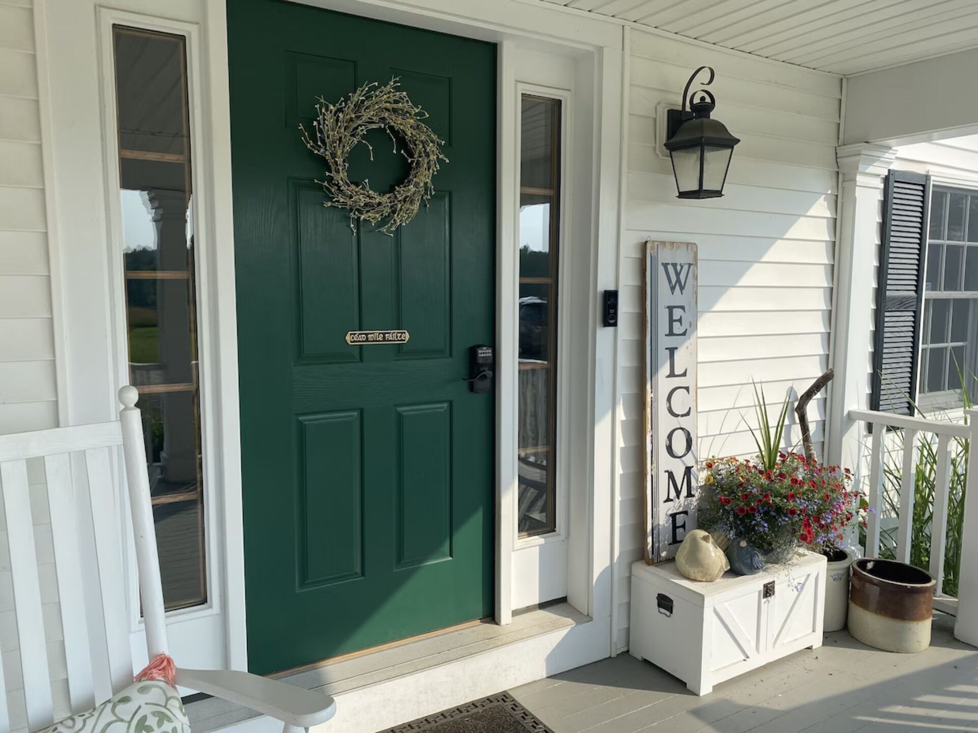 A green door with a wreath, a welcome sign, and a planter with flowers.