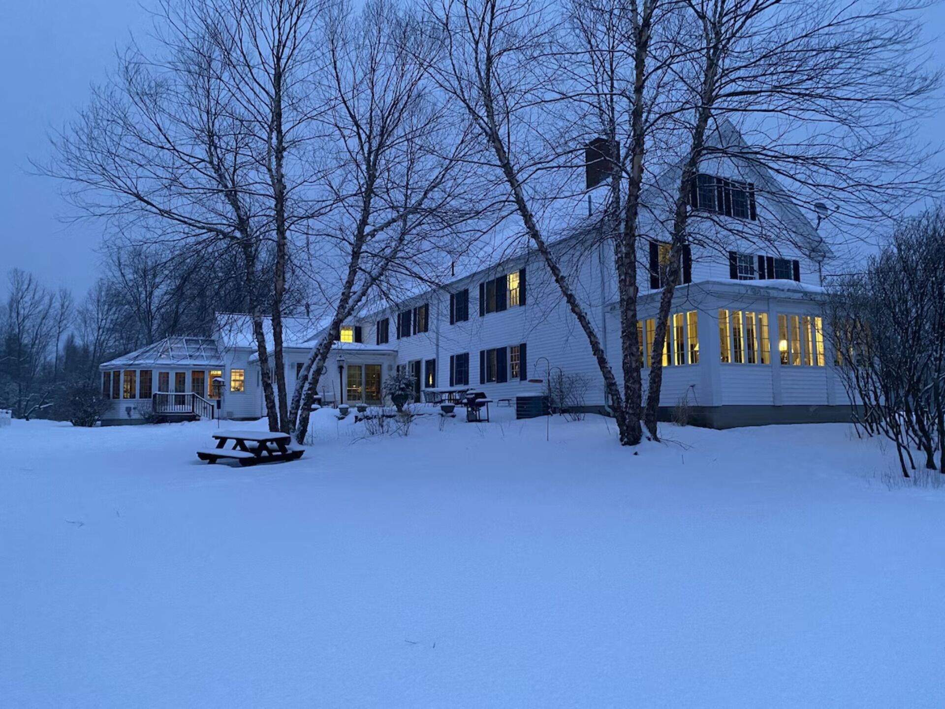 Ett stort hus i två våningar med en snötäckt gräsmatta, en inglasad uteplats och en synlig skorsten.