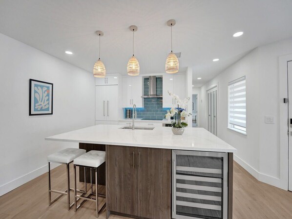 A modern kitchen with a white island, pendant lights, and a view into the dining area. - Villa Azul | 4-Min Walk to Beach & Beside Atlantic (Delray Beach)