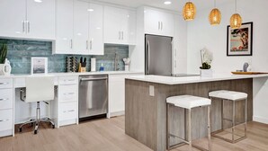 A modern kitchen with white cabinets, a stainless steel refrigerator, and a central island with bar stools.