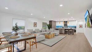 A modern living room with a dining area, a sofa, and a kitchen in the background. - Villa Nicole: 4-min walk to beach, off of Atlantic (Delray Beach)
