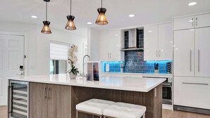 A modern kitchen with a central island, white cabinetry, and pendant lighting. - Villa Lauren: 4-min walk to beach, off of Atlantic (Delray Beach)