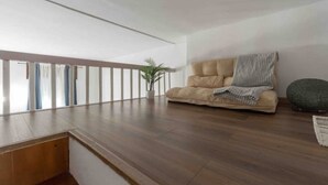 A spacious room with a wooden floor, a beige sofa with a striped throw, and a potted plant. - Enjoy a stay in the Vittoria home just 15 minutes from Milan Cathedral. (Milano)