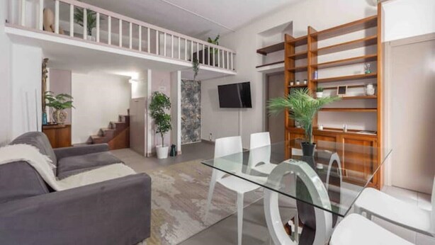 A modern living room with a glass dining table, grey sofas, and a wooden bookshelf. - Enjoy a stay in the Vittoria home just 15 minutes from Milan Cathedral. (Milano)