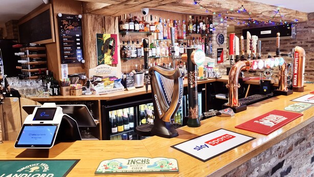Uma área de bar com diversos tipos de bebidas, uma torneira de chopp e um terminal de pagamento digital.