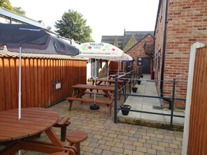 An outdoor patio area with wooden tables and benches, a covered seating area, and a brick building in the background. - Oddfellows Hotel Bar & Restaurant (Goole)