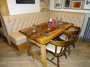 A dining area with a wooden table set for six, surrounded by wooden chairs with cushioned seats. A cushioned bench is positioned along the wall, and a framed picture hangs above the table. - Oddfellows Hotel Bar & Restaurant (Goole)
